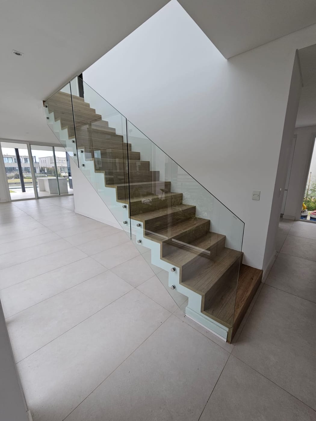 Escalera de madera con baranda de vidrio templado y botones, living con vista a pileta