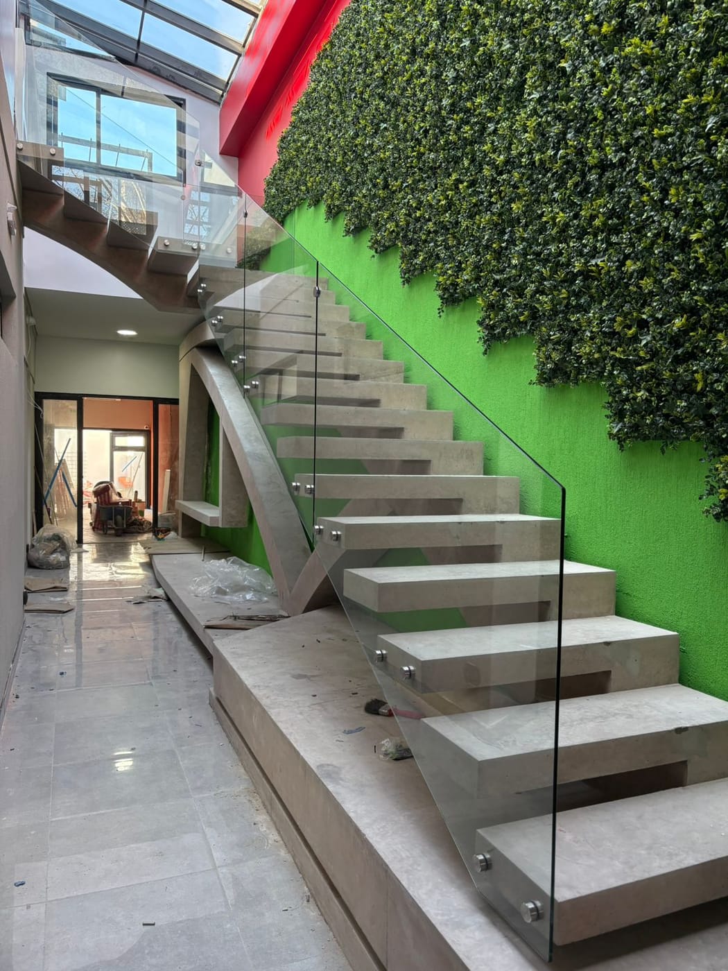 Baranda de vidrio templado con botones junto a muro verde artificial y estructura de acero