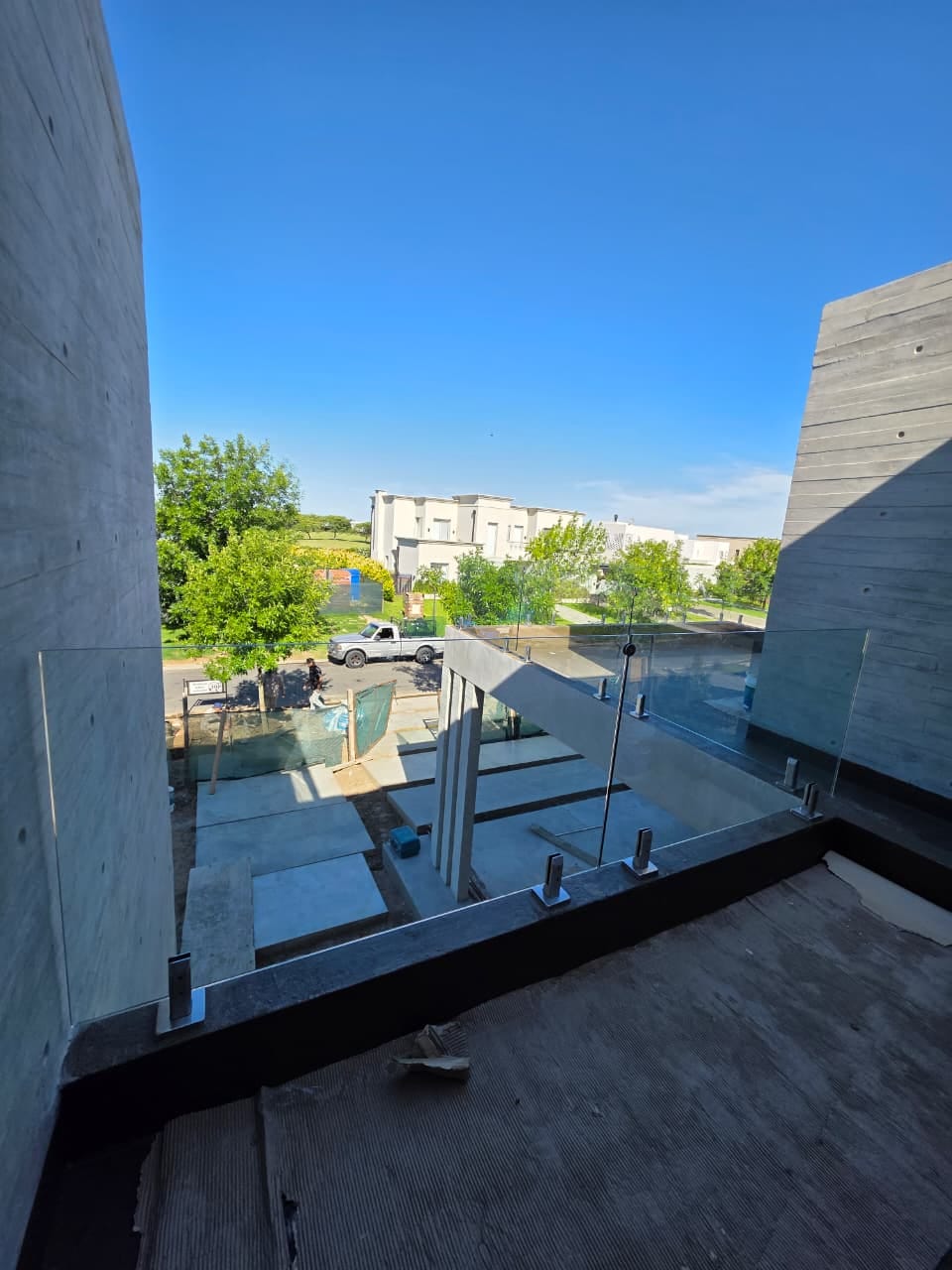 Vista de baranda de vidrio con minipostes sobre balcón, de fondo pileta en construcción